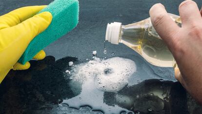 Caucasian man, with a green sponge in his hand and yellow gloves, adds vinegar to baking soda to clean a surface.