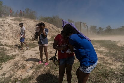 Niñas se cubren del polvo levantado por el helicóptero con una sombrilla.