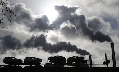 Un camión con coches atraviesa un puente de París ante el humo de una fábrica 