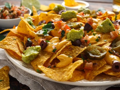 A plate of nachos with guacamole, cheese, olives and jalapeño peppers.