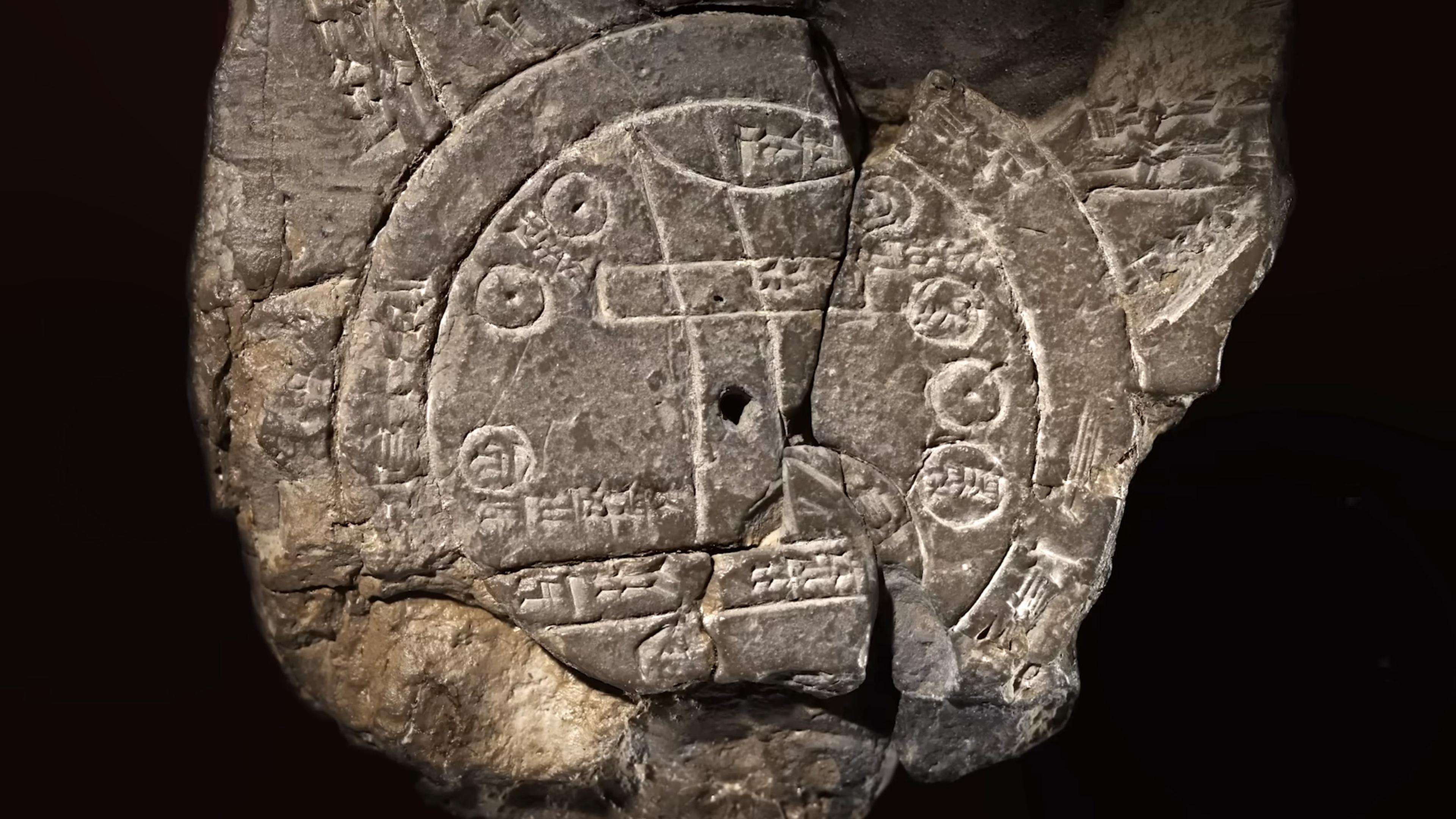 An ancient, broken clay tablet with a circular design and various inscriptions, displayed on a dark background.