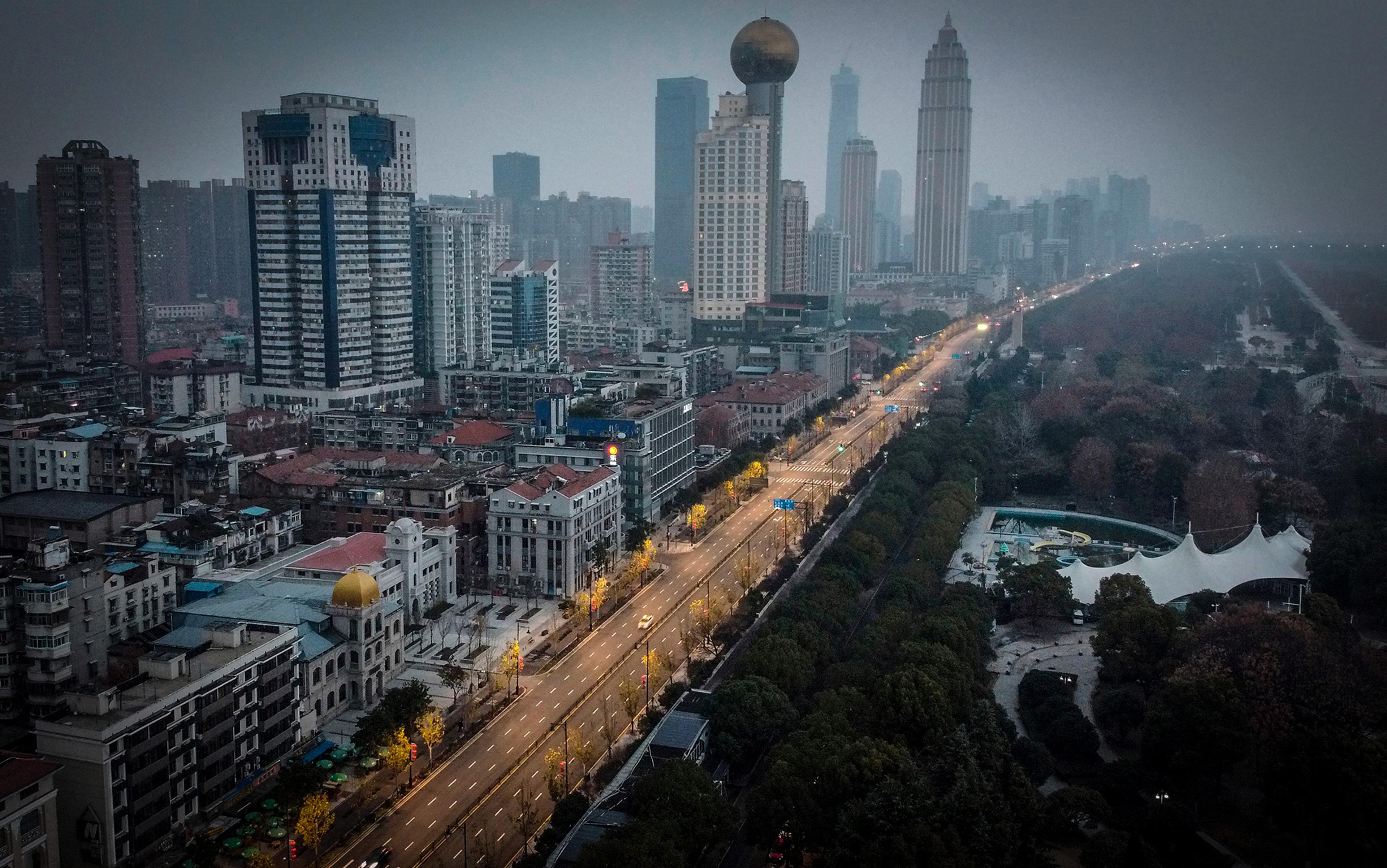 Aerial photo of a cityscape with tall buildings, a large spherical structure, an empty wide road and trees lining a park area on the right.