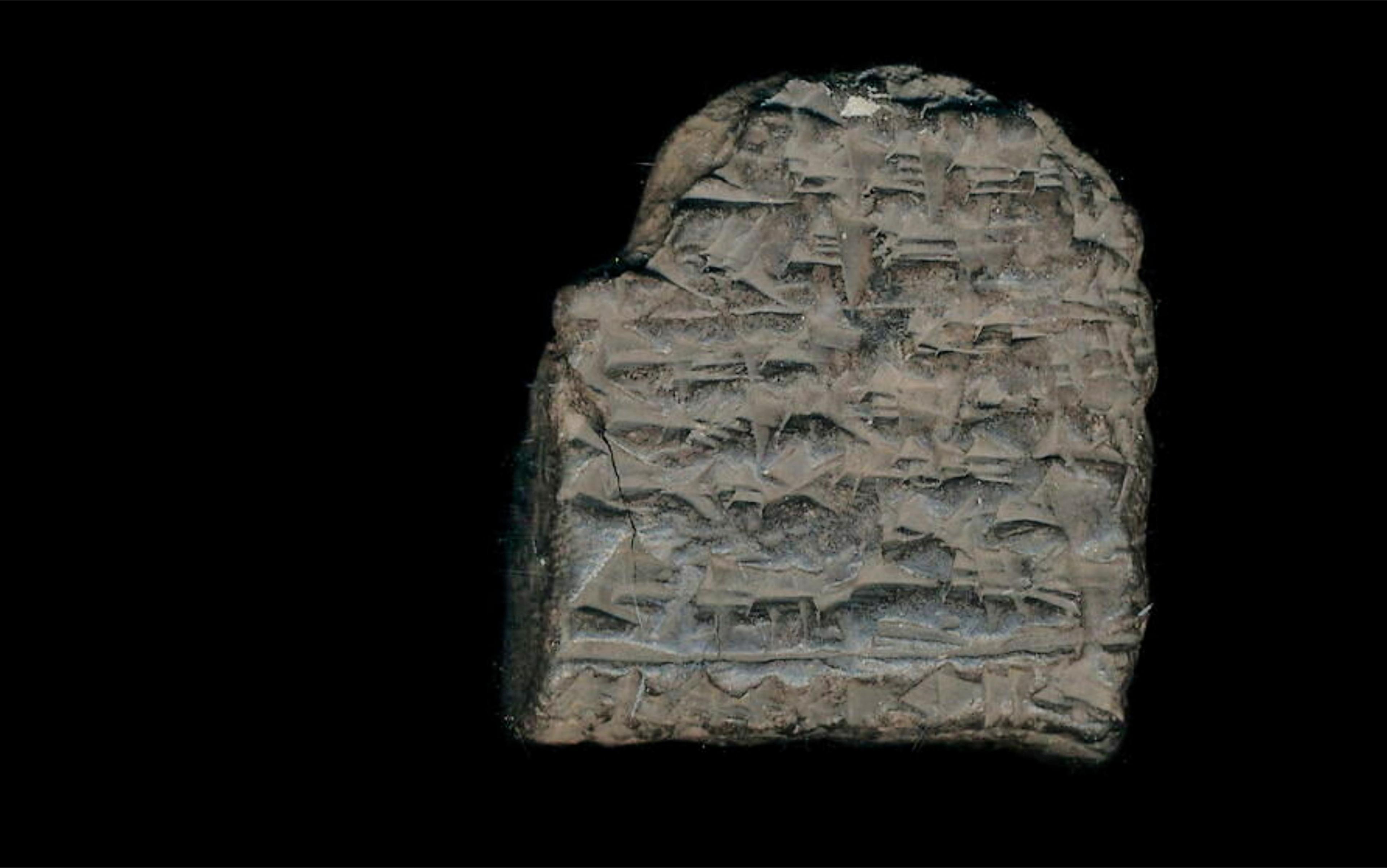 Ancient cuneiform script inscribed on a worn, rectangular clay tablet set against a black background.