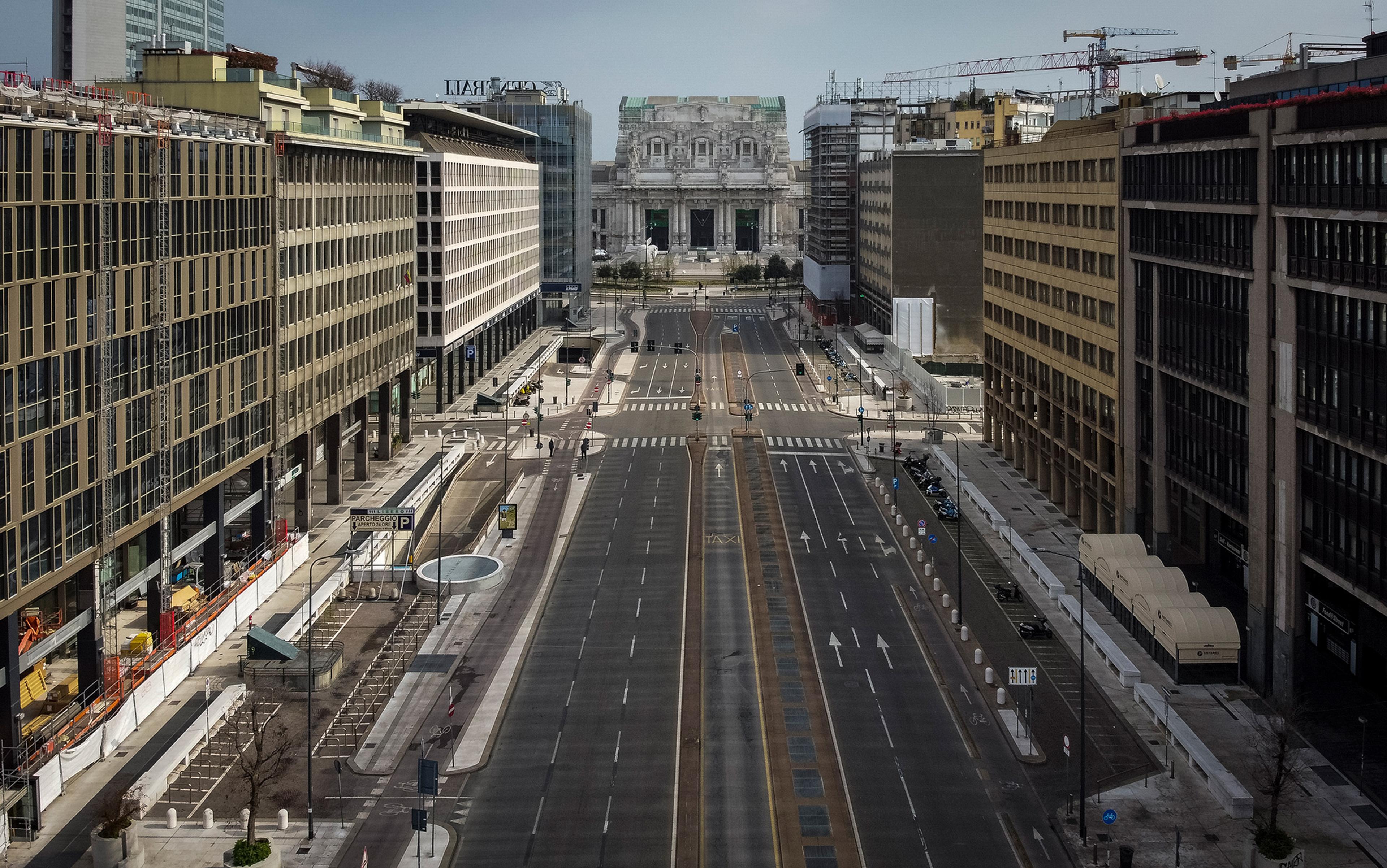 A deserted city street flanked by tall buildings, leading to a large historic building in the background under a clear sky.