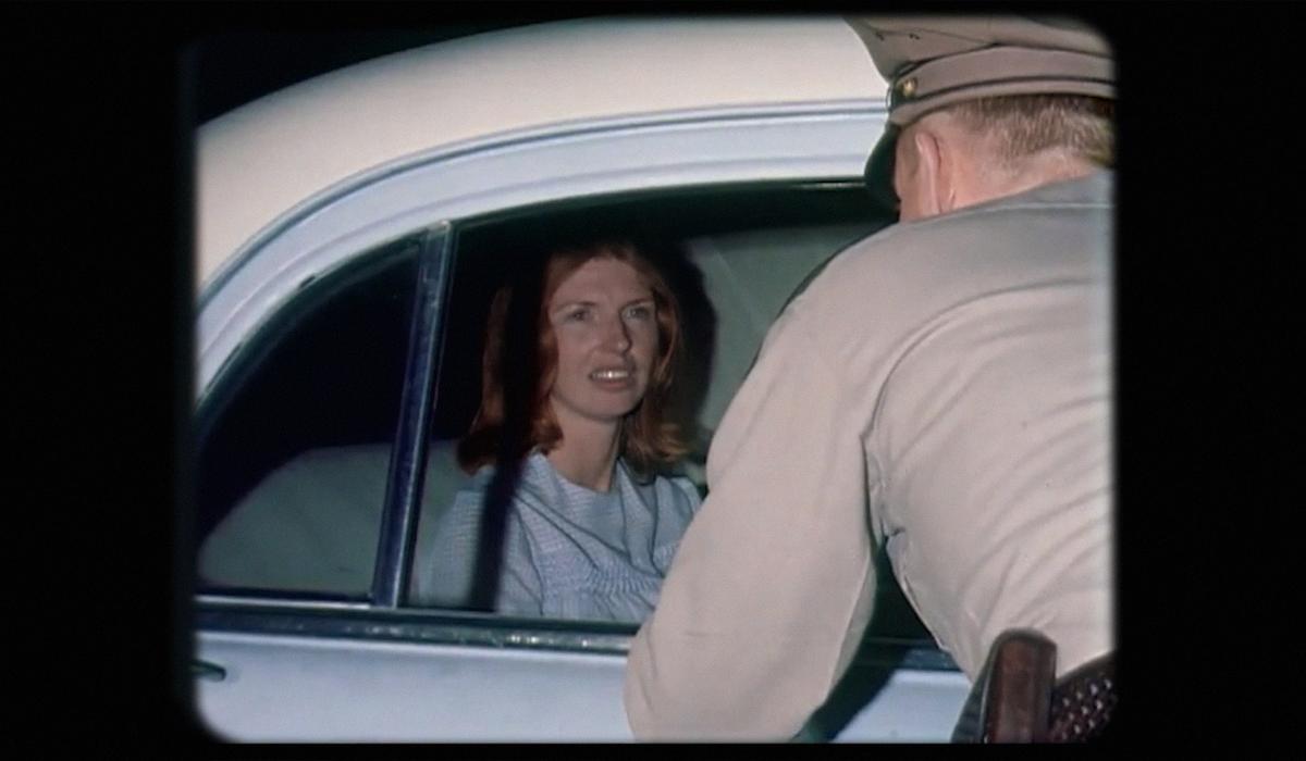 A woman inside a car is talking to a man in a uniform leaning into the vehicle through the window, vintage image.