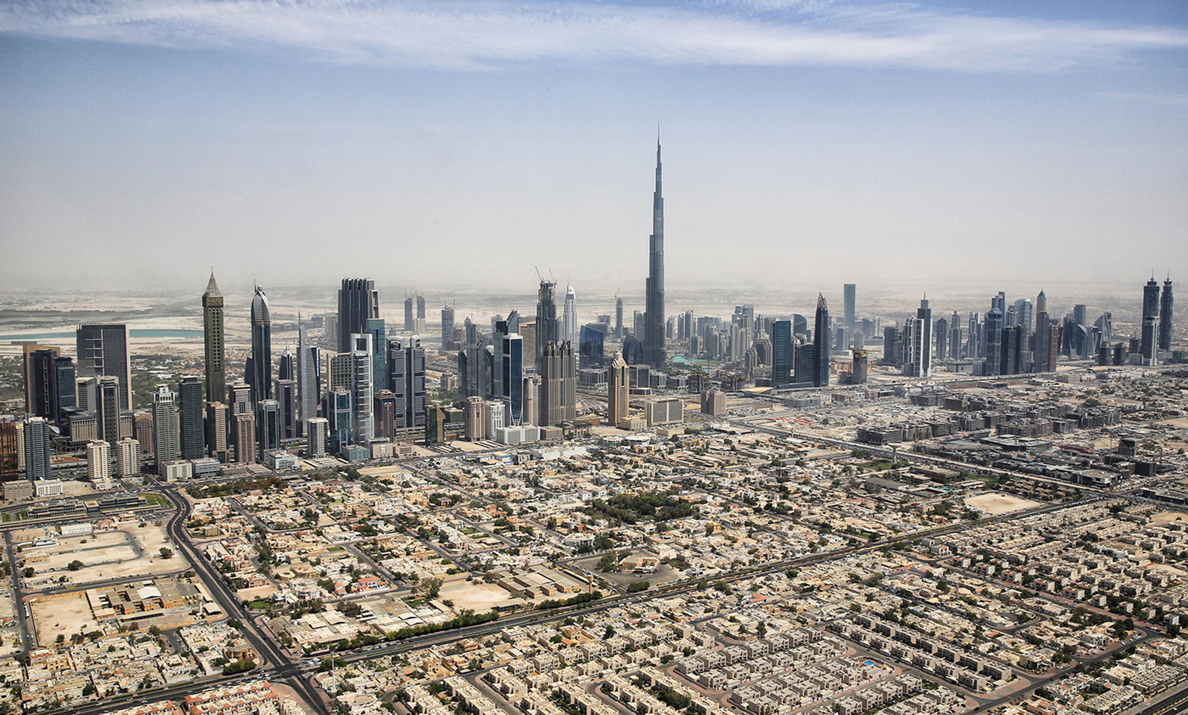 Aerial photo of a city skyline with numerous skyscrapers and a mix of residential buildings in the foreground, under a hazy sky.