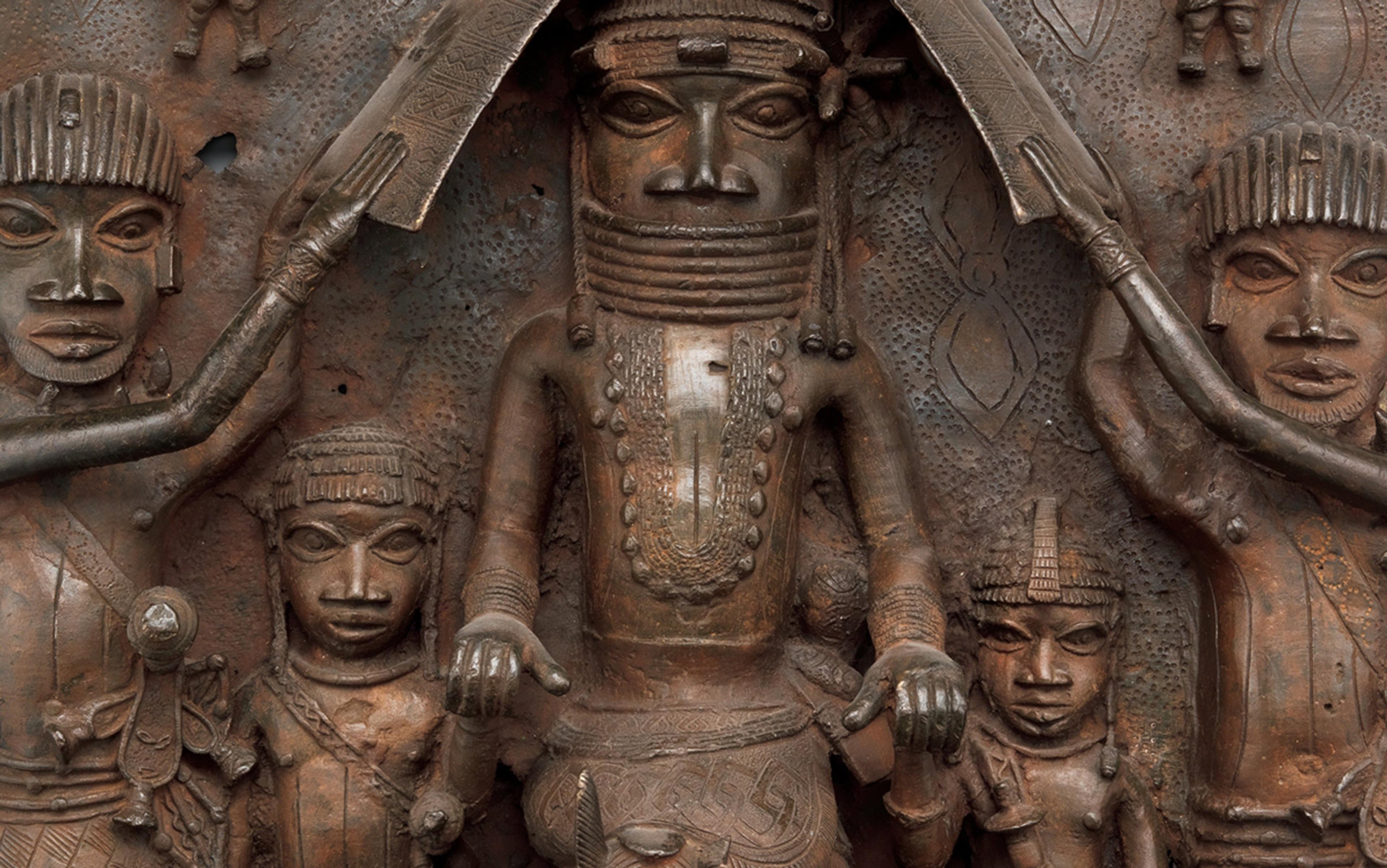 Bronze plaque with intricate carvings depicting figures in traditional attire, showing detailed facial expressions and body ornaments in a historical style.