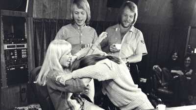 Abba-yhtyeen jäsenet ovat musiikkistudiossa. Björn Ulvaeus ja Benny Andersson seisovat. Agnetha Fältskog istuu miksauspöydän ääressä ja nauraa, kun Anni-Fris Lyngstad on painautumassa pää edellä hänen syliinsä.