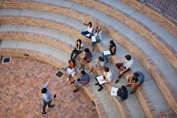 Students taking classes in an outdoor auditorium while using 8x8 solutions on mobile devices