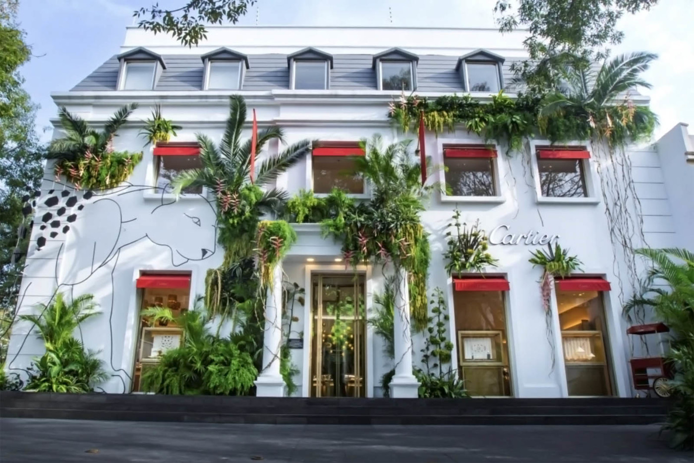 Photograph of a white building with lots of foliage and a mural of a wild cat.