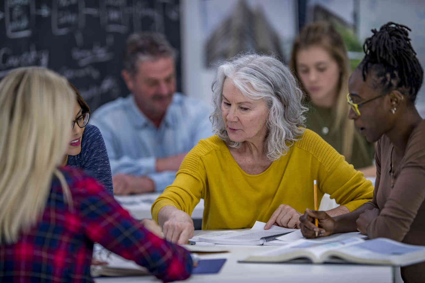 A group of adult students works from textbooks at a table. 