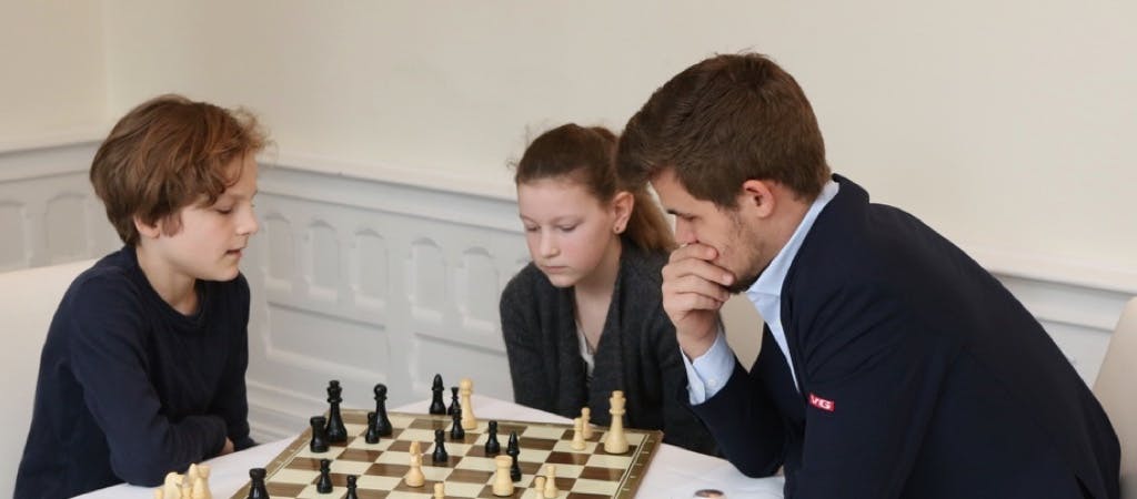 Image of Magnus Carlsen teaching two children to play Chess