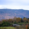 Des éoliennes en haut d'une montagne dans un paysage coloré d'automne. Au bas de la montagne, il y a une maison.