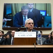 Merrick Garland, devant un porte-nom; on distingue derrière lui des gens et un écran de télévision géant. 