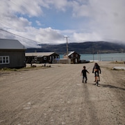 Une jeune fille fait de la bicyclette et un garçon court à côté d'elle dans une rue de Pangnirtung, en août 2023.