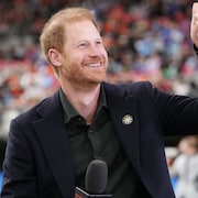 Le prince Harry tient un micro et lève le pouce en souriant.