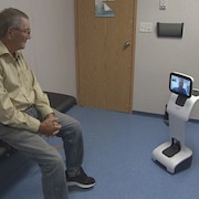 Un homme assis dans une salle d'examen devant un petit robot.