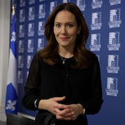 La journaliste Véronique Prince est dans un bureau à l'Assemblée nationale du Québec. Elle est debout et regarde l'objectif de la caméra. Elle se prépare à expliquer son sujet. 