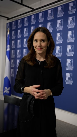 La journaliste Véronique Prince est dans un bureau à l'Assemblée nationale du Québec. Elle est debout et regarde l'objectif de la caméra. Elle se prépare à expliquer son sujet. 