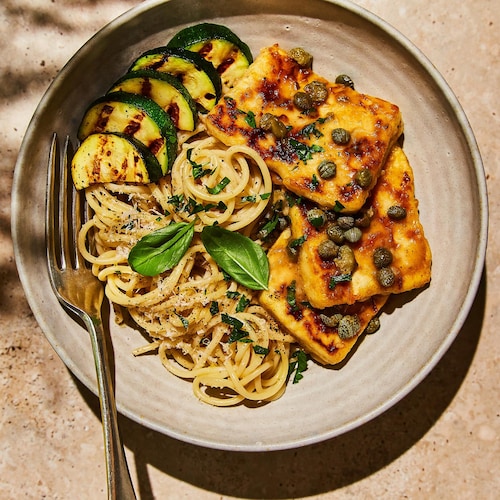 Du tofu piccata dans une assiette avec des morceaux de courgette de ses spaghettis.