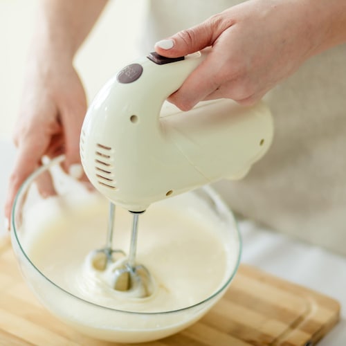 Une personne mélange de la crème à l'aide d'un batteur à main.