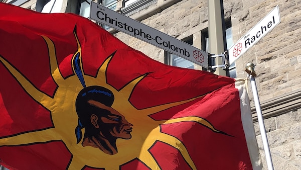 Une drapeau warrior flotte au vent sous un panneau de rue au nom de Christophe Colomb à Montréal.