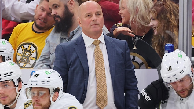 Un homme qui porte un complet se tient debout derrière le banc d'une équipe de hockey.