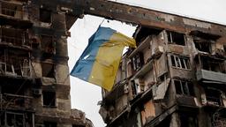 Eine zerrissene ukrainische Flagge hängt an einem Draht vor einem Wohnhaus, das während des russischen Angriffskrieges in der südukrainischen Hafenstadt Mariupol am 14. April 2022 zerstört wurde.