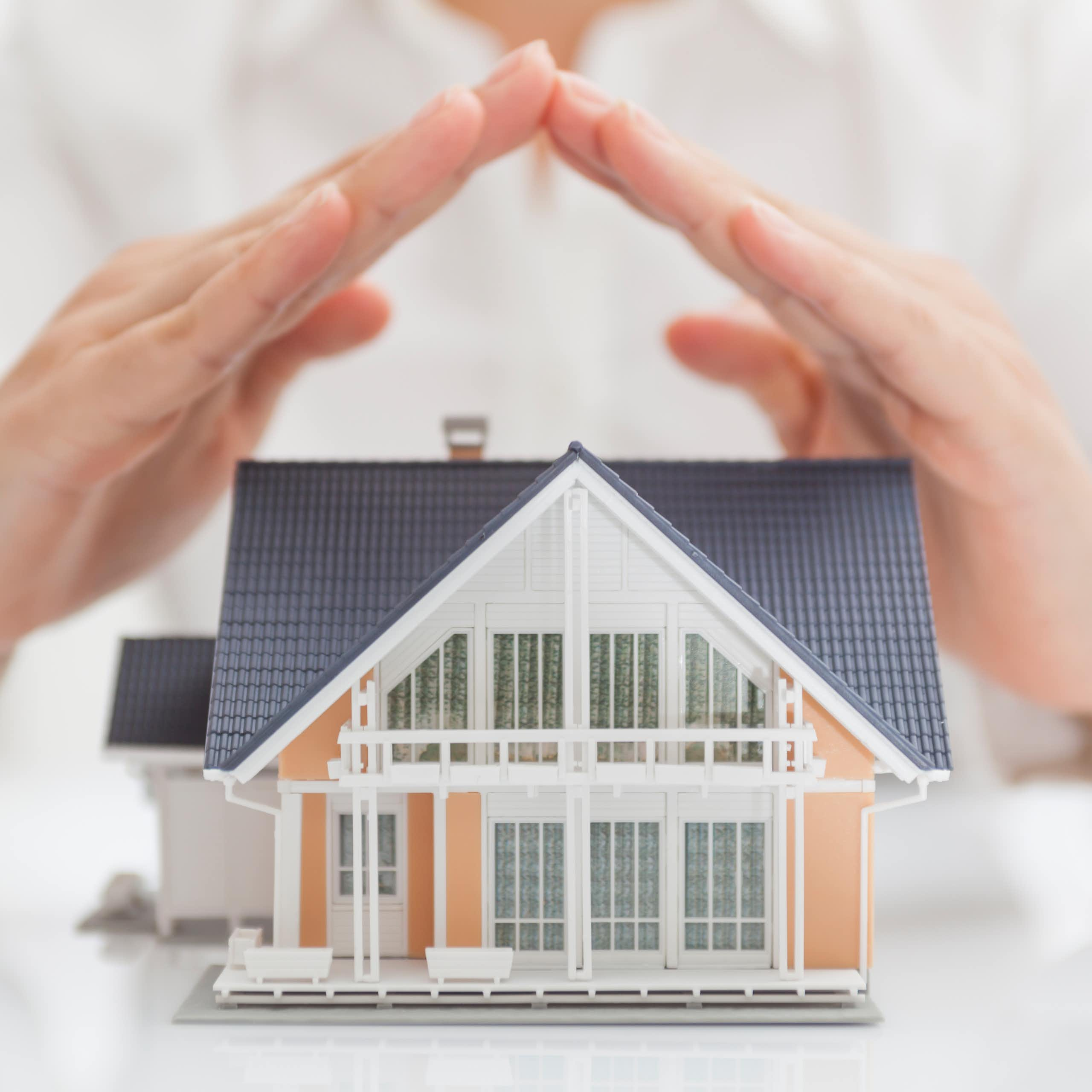 A person holds their hands over a dollhouse, as if shielding it from rain.