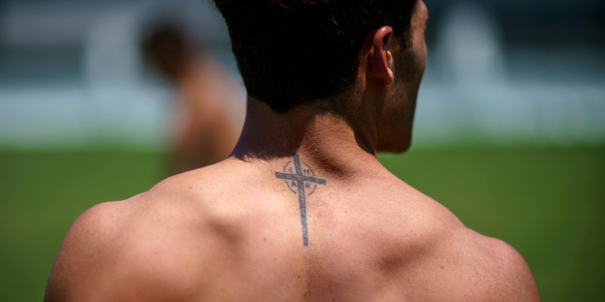 The upper back and neck of a shirtless man, with a cross tattoo visible.