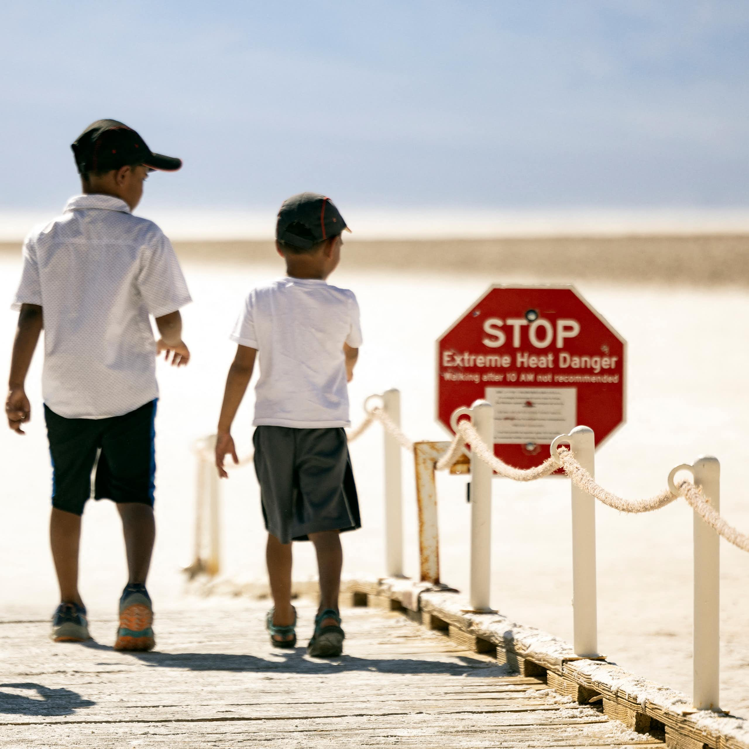 A man and two young boys walk toward a desert landscape, passing a sign that says "Stop: Extreme Heat Danger"