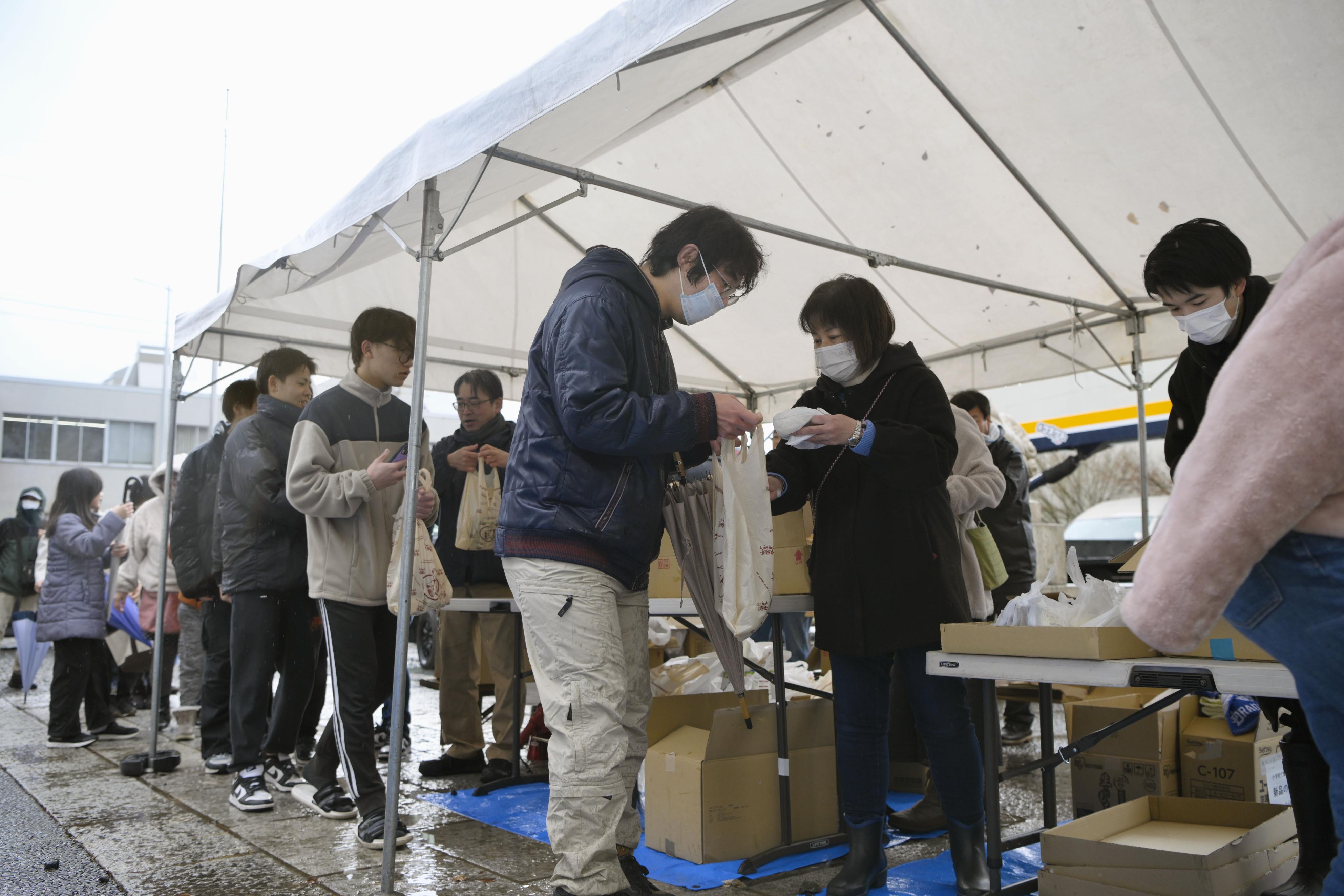 石川県輪島市の重蔵神社で、年越しそばなどが入った袋を受け取る人たち＝30日午後