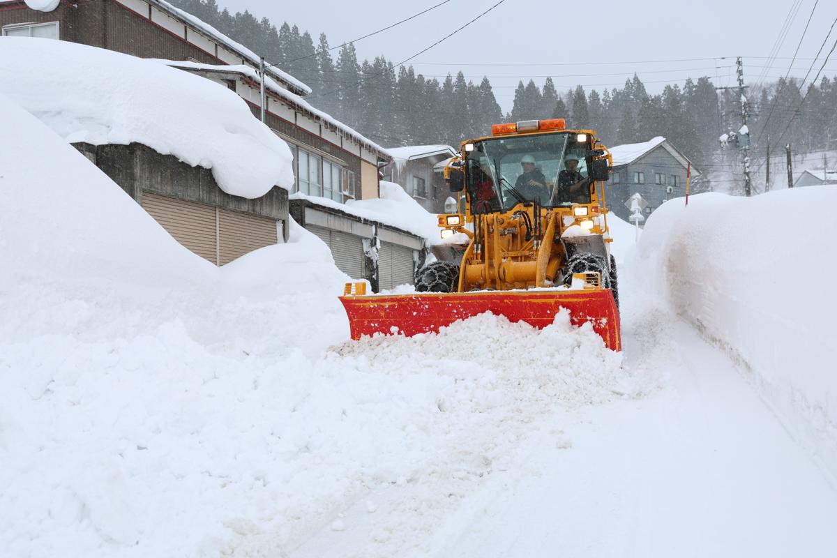 雪の壁の間で続けられる除雪作業＝２月８日、長岡市山古志竹沢