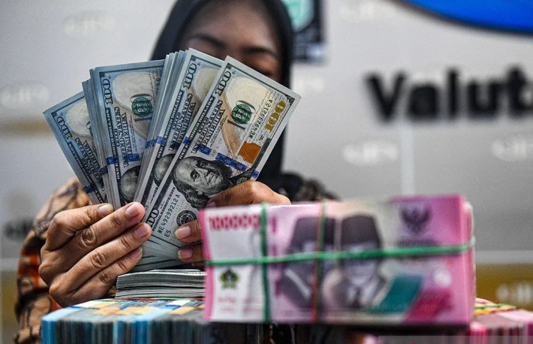 Double bill: A teller counts United States dollar and rupiah bills on March 1, 2024 at a money changer in Jakarta. 