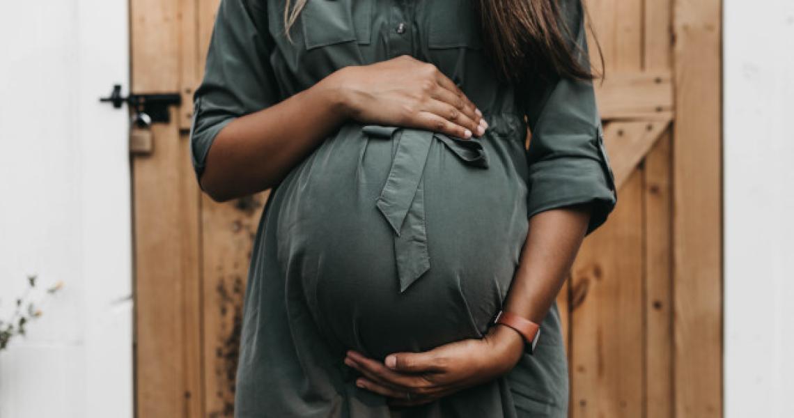 A pregnant Black woman holding her stomach.