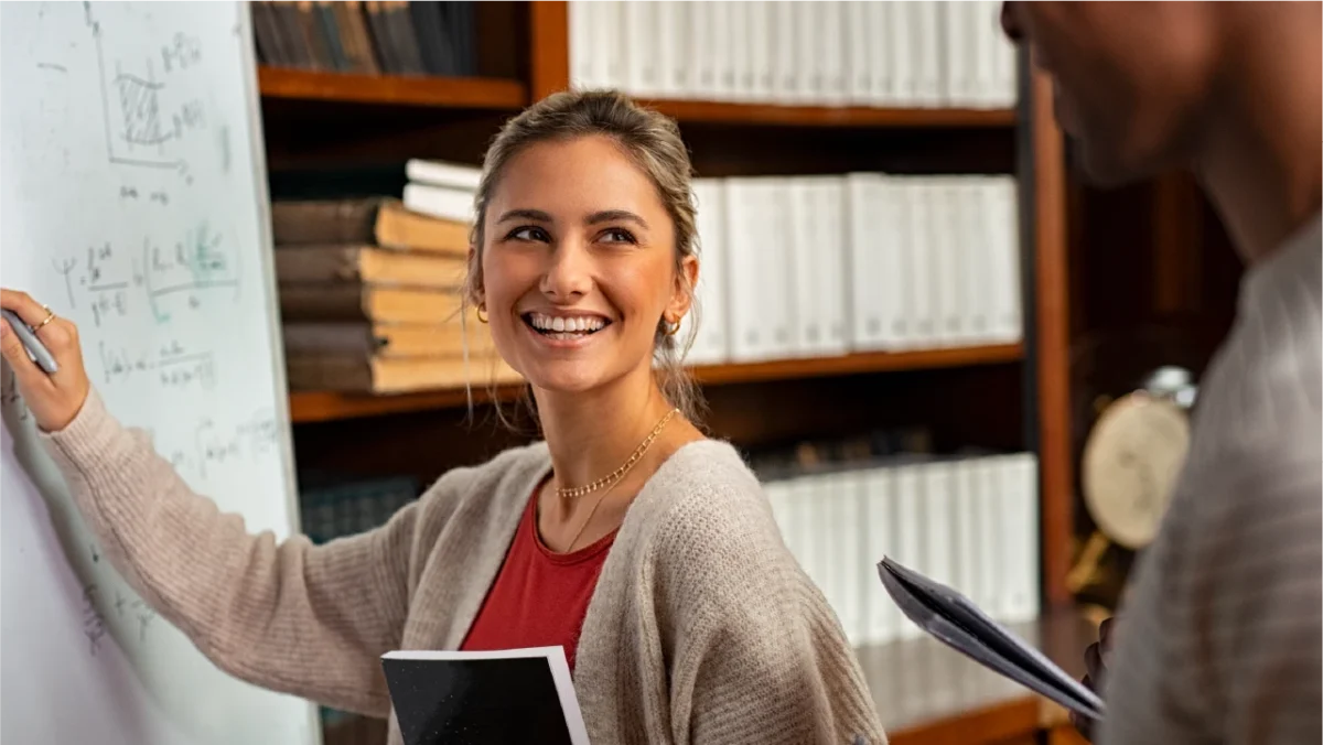 A smiling woman engaged in writing on a whiteboard, showcasing a positive and interactive learning environment.