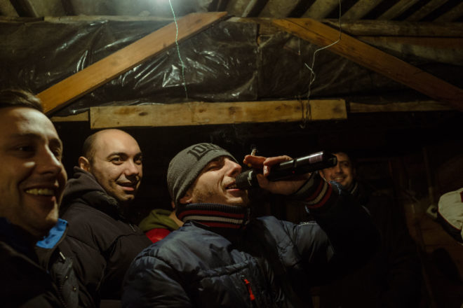 Men gather in a garden shed for moonshine and winter caroling. Holding the mic is a resident who profited from political websites.
