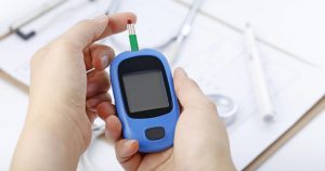 mãos utilizando dispositivo de detecção de diabetes com instrumentos clínicos ao fundo