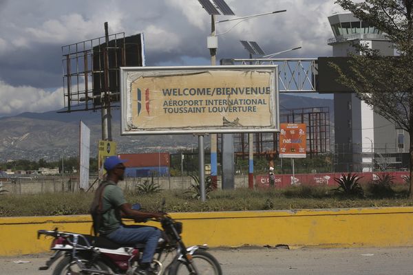 Un homme passe sa moto devant l'aéroport Toussaint Louverture le jour de sa réouverture à Port-au-Prince, Haïti, le mercredi 11 décembre 2024.