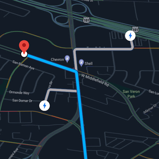 Google Maps shown behind a car at a charging station. The map shows charging stations on the current route.