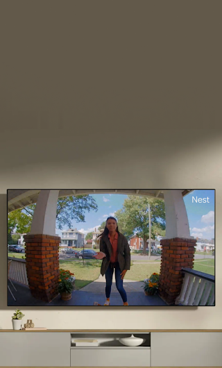 A TV in a living room showing a delivery person standing on a stoop waving to the doorbell camera.