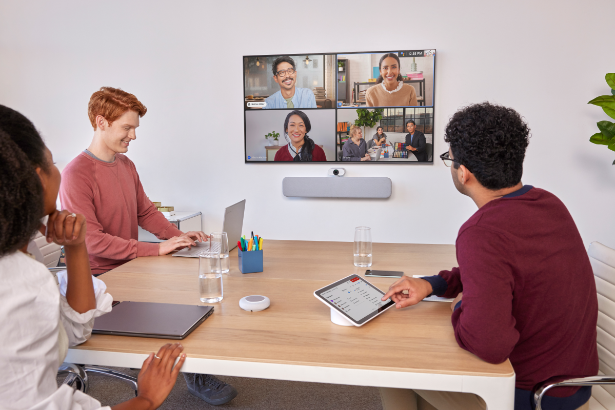 Une salle de réunion avec trois personnes présentes et quatre participants affichés sur l'écran de visioconférence