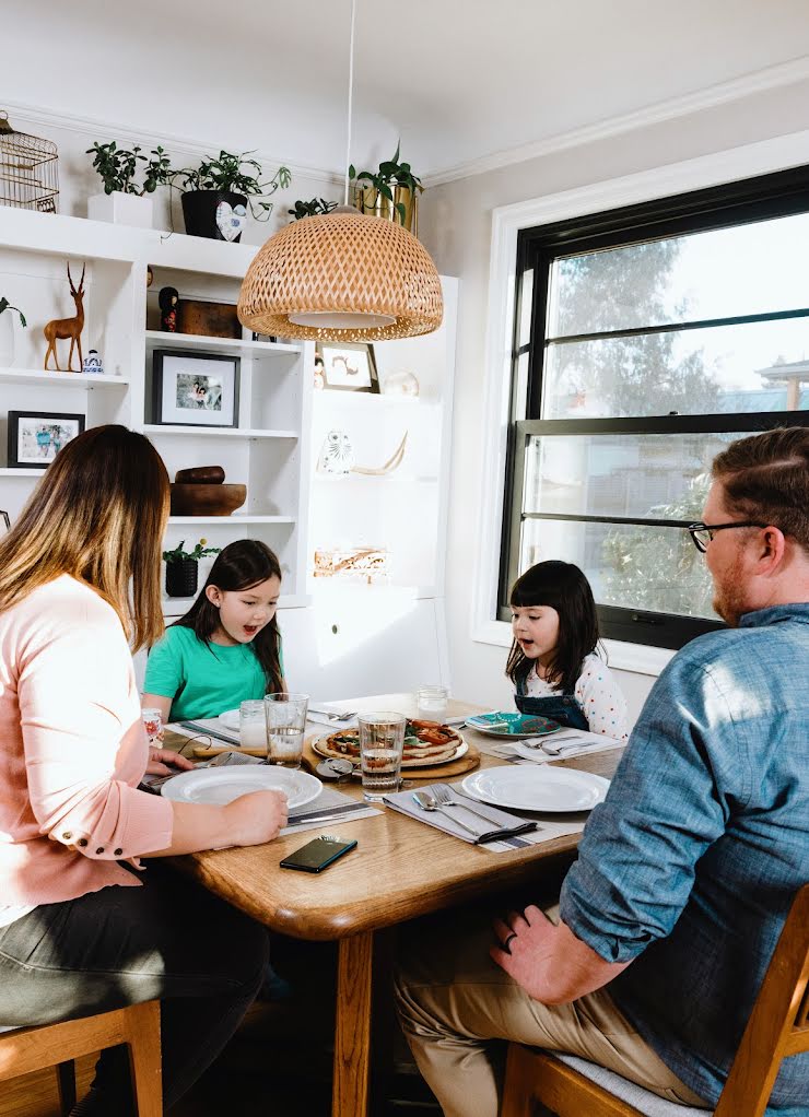 A family sits at a dining room table, a pizza in the middle, a phone in between the two parents.