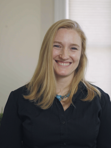 Person with long blond hair and black shirt and turquoise necklace smiling.