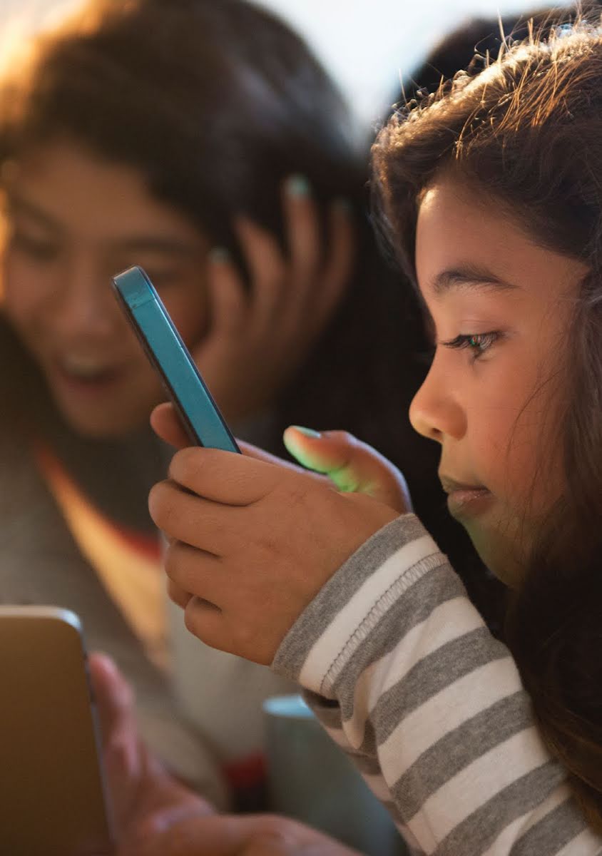 A young girl looks inquisitively into her phone with a group of friends.