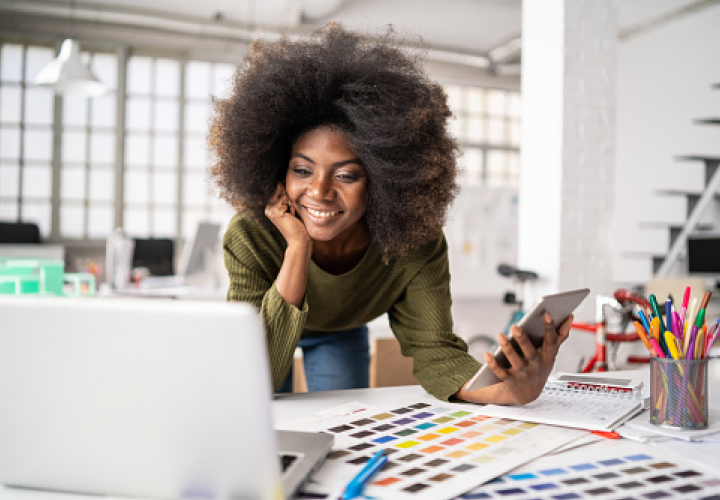 Une femme dans un bureau regardant son ordinateur et tenant une tablette. 