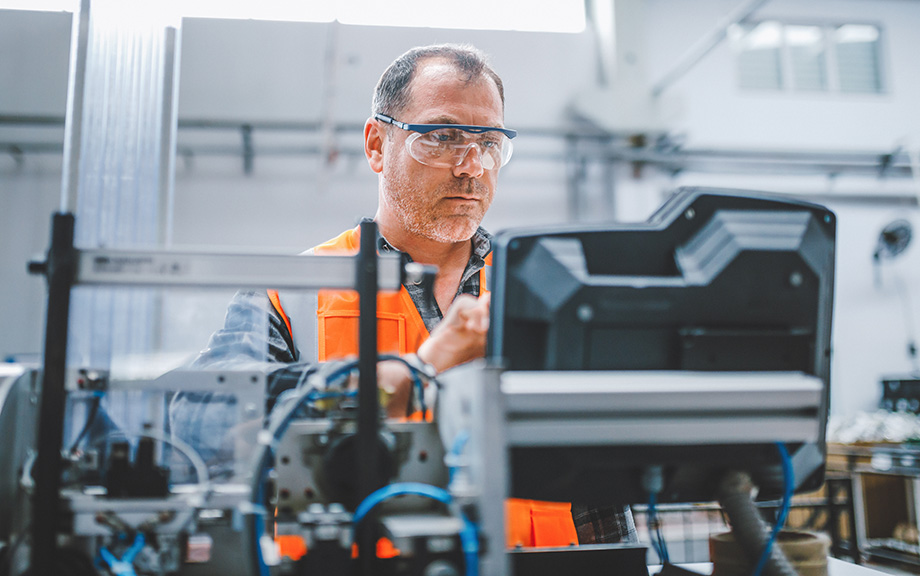 photo: Male industrial worker working with manufacturing equipment in a factory.