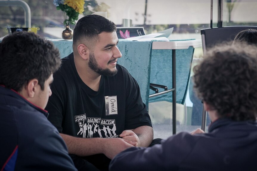 Man in black top sitting in a group with students.