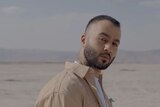 Head shot of Iranian man looking at the camera but body facing to the right with a desert background.