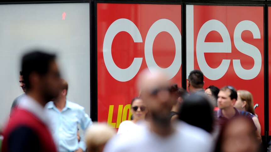 A crowd of out-of-focus people walk in front of a large in-focus Coles supermarket sign.